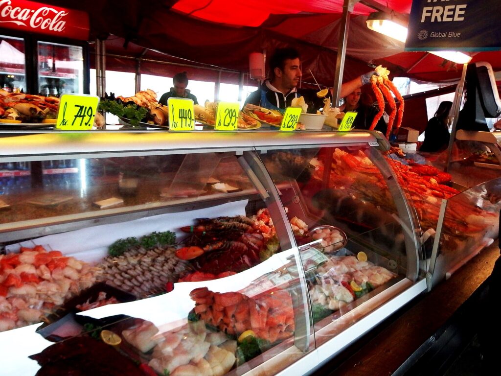 Selger bak en disk med ferdige sjømatretter på Fisketorget i Bergen